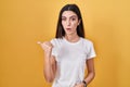Young beautiful woman standing over yellow background surprised pointing with hand finger to the side, open mouth amazed Royalty Free Stock Photo