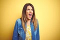 Young beautiful woman standing over yellow isolated background angry and mad screaming frustrated and furious, shouting with anger