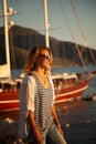 Young beautiful woman standing on the seashore next to a yacht at sunset, vacation and summer sea travel Royalty Free Stock Photo