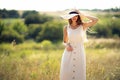 young beautiful woman stands on field in summer while wearing a sunhat and midi dress. Lifestyle