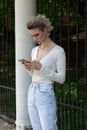 Young beautiful woman stands with a phone outside in blue jeans Royalty Free Stock Photo