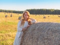 Young beautiful woman is staying near haystack at summer day