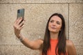 Young beautiful woman with straight brown hair and orange top, making a video call with her cell phone. Concept fashion, beauty, Royalty Free Stock Photo