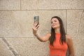 Young beautiful woman with straight brown hair and orange top, making a video call with her cell phone. Concept fashion, beauty, Royalty Free Stock Photo