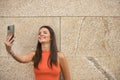 Young beautiful woman with straight brown hair and orange top, making a video call with her cell phone. Concept fashion, beauty, Royalty Free Stock Photo