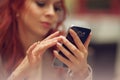 Young beautiful woman in a street cafe, is busy with her cell phone, close up at hands holding mobile phone Royalty Free Stock Photo