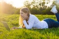 Young beautiful woman student with a laptop lies on the grass in sunset Royalty Free Stock Photo