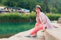 A young beautiful woman in summer clothes and a straw hat sitting at steps of river pier. Summer vacation and relax Royalty Free Stock Photo