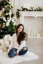 Young beautiful woman in sweater and blue jeans sitting on floor near christmas tree Royalty Free Stock Photo