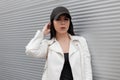 Young beautiful woman in a T-shirt in a white stylish leather jacket in a fashionable black cap poses Royalty Free Stock Photo