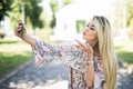 Young beautiful woman takes selfie on cell phone sitting on grass in summer city park. Blow kiss. Outdoor Royalty Free Stock Photo