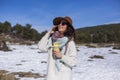 Young beautiful woman talking on her mobile phone in the snow and holding a cup of tea or coffee. Outdoors portrait, lifestyle Royalty Free Stock Photo