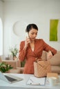 Young beautiful woman talking on mobile phone and using her laptop while standing at her working place Royalty Free Stock Photo
