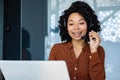 Young beautiful woman talking to customers remotely, african american female worker smiling using headset phone and Royalty Free Stock Photo
