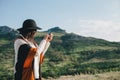 Young beautiful woman traveler wearing hat and poncho taking pictures on her smart phone Royalty Free Stock Photo