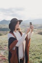 Young beautiful woman traveler wearing hat and poncho taking pictures on her smart phone Royalty Free Stock Photo