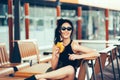 Young beautiful woman in trendy sunglasses eating burger and enjoying while sitting outdoor and waiting for friends. Fastfood Royalty Free Stock Photo
