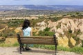 A young beautiful woman in a turquoise dress sits on a wooden bench on a hill against the blurred landscape of mountain caves in