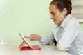 A young beautiful woman uses a digital tablet at home, sitting at her workplace, a cheerful smiling girl. Technology, business, Royalty Free Stock Photo