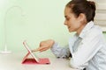 A young beautiful woman uses a digital tablet at home, sitting at her workplace, a cheerful smiling girl. Technology, business, Royalty Free Stock Photo