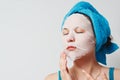 A young beautiful woman uses a fabric cosmetic face mask with a towel wrapped around her head Royalty Free Stock Photo