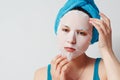 A young beautiful woman uses a fabric cosmetic face mask with a towel wrapped around her head Royalty Free Stock Photo