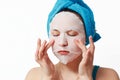 A young beautiful woman uses a fabric cosmetic face mask with a towel wrapped around her head Royalty Free Stock Photo