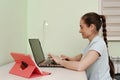 A young beautiful woman uses a laptop while sitting at her workplace, a cheerful smiling girl. Technology, business, homework, Royalty Free Stock Photo