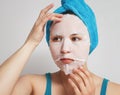 A young beautiful woman uses a moisturizing cosmetic fabric face mask with a towel wrapped around her head. on white background Royalty Free Stock Photo