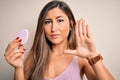 Young beautiful woman using beauty sponge with facial makeup over pink background with open hand doing stop sign with serious and Royalty Free Stock Photo