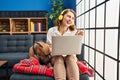 Young beautiful woman using laptop sitting on the sofa pointing thumb up to the side smiling happy with open mouth Royalty Free Stock Photo