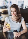 Young beautiful woman using smart phone in a cafe. Pretty student girl sitting in a coffee shop and typing on mobile phone Royalty Free Stock Photo