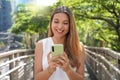 Young woman using smartphone in a city. Smiling elegant girl texting on mobile phone outdoor. Modern lifestyle, Royalty Free Stock Photo