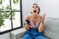 Young beautiful woman using smartphone typing message sitting on the sofa crazy and mad shouting and yelling with aggressive Royalty Free Stock Photo