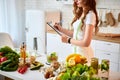 Young beautiful woman using tablet while cooking in the modern kitchen. Healthy eating, vitamins, dieting, technology and people Royalty Free Stock Photo