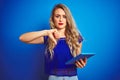 Young beautiful woman using tablet over blue isolated background with angry face, negative sign showing dislike with thumbs down, Royalty Free Stock Photo