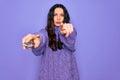 Young beautiful woman using television remote control over isolated purple background pointing with finger to the camera and to Royalty Free Stock Photo
