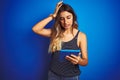 Young beautiful woman using touchpad tablet over blue isolated background stressed with hand on head, shocked with shame and Royalty Free Stock Photo