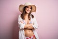 Young beautiful woman on vacation wearing bikini and summer hat over pink background happy face smiling with crossed arms looking Royalty Free Stock Photo