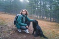 Young beautiful woman walking in autumn cloudy forest with her black dog Royalty Free Stock Photo