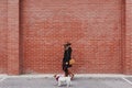 Young beautiful woman walking with her dog by the street. Orange brick wall background. Love and pets outdoors