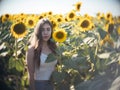 Young beautiful woman walks across field in sun. Yellow sunflowers and blue sky. Portrait view Royalty Free Stock Photo