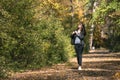 Young beautiful woman walks along the alley of an autumn park and enjoys a warm day. Lonely girl walk through the forest Royalty Free Stock Photo