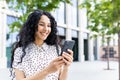 A young beautiful woman walks through the city with a phone in her hands, smiles contentedly, uses a smartphone Royalty Free Stock Photo