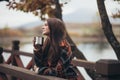 Young beautiful woman in a warm classic coat drinking tea near lake Royalty Free Stock Photo