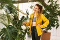 Young beautiful woman watering flowers and plants in her home garden or in a greenhouse, smiling and looking at the camera Royalty Free Stock Photo