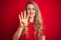Young beautiful woman wearing basic t-shirt standing over red isolated background showing and pointing up with fingers number four