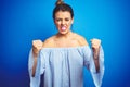 Young beautiful woman wearing bun hairstyle over blue isolated background angry and mad raising fists frustrated and furious while