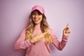 Young beautiful woman wearing cap over pink isolated background smiling and looking at the camera pointing with two hands and Royalty Free Stock Photo