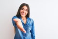 Young beautiful woman wearing casual denim shirt standing over isolated white background smiling friendly offering handshake as Royalty Free Stock Photo